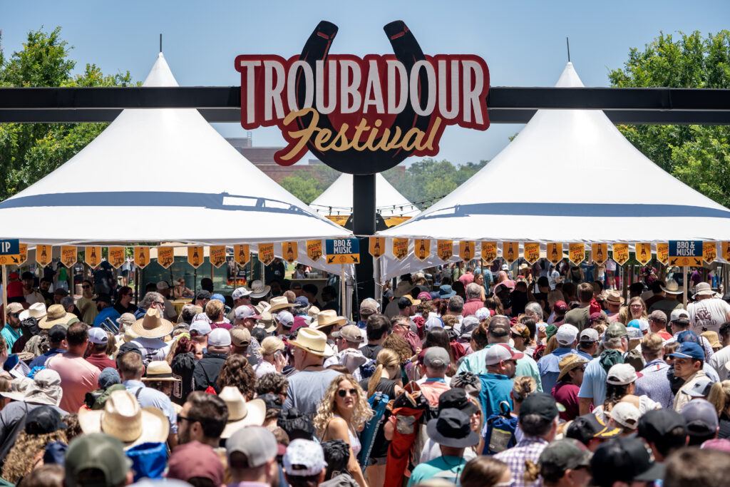 An image showcasing a gathering of individuals beneath a sign stating Troubadour Festival.