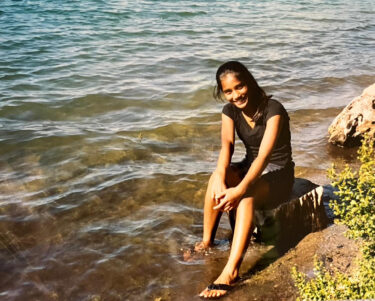 A girl sits on a rock with her feet in water