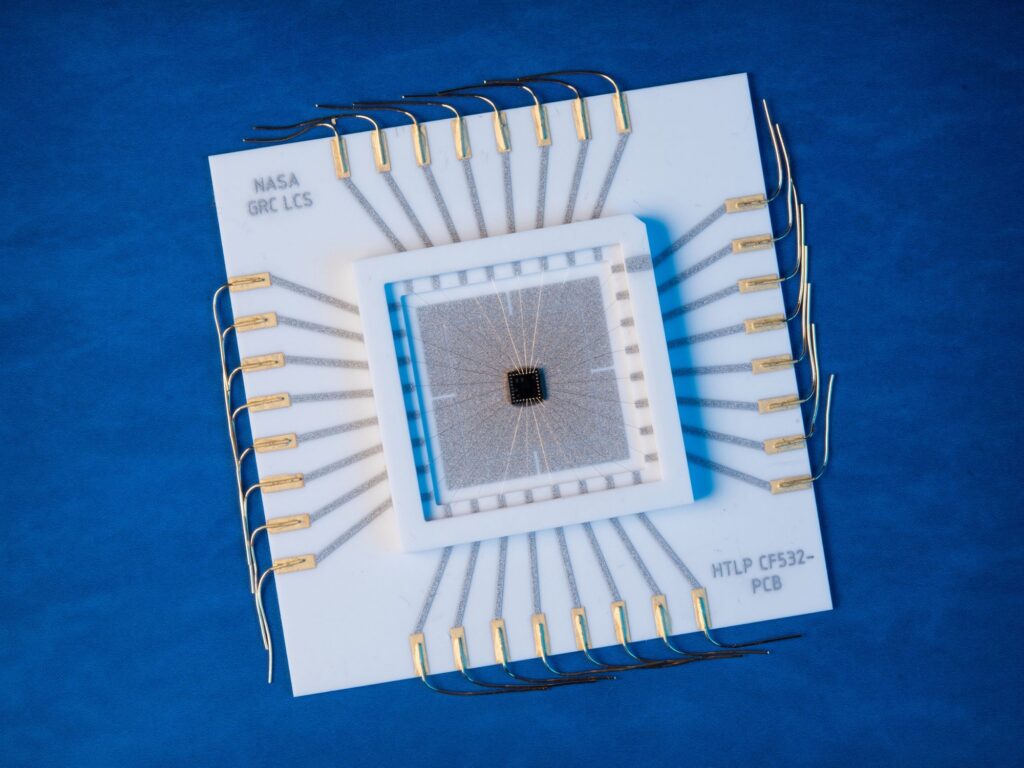 A black square at the center surrounded by larger lighter squares. Thin metallic bands extend from the center in a floral pattern with four petals. The device is placed against a blue backdrop.