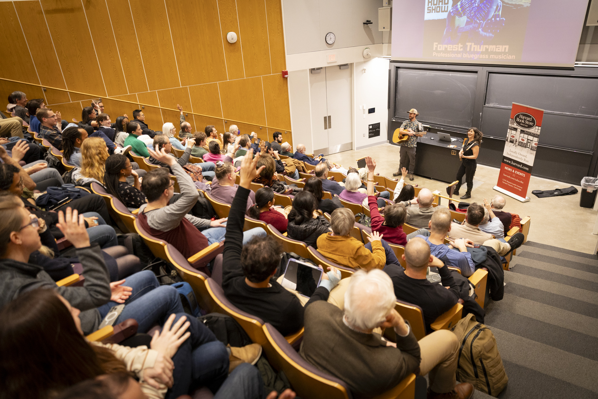Audience members raising their hands in response to a survey about bluegrass music.