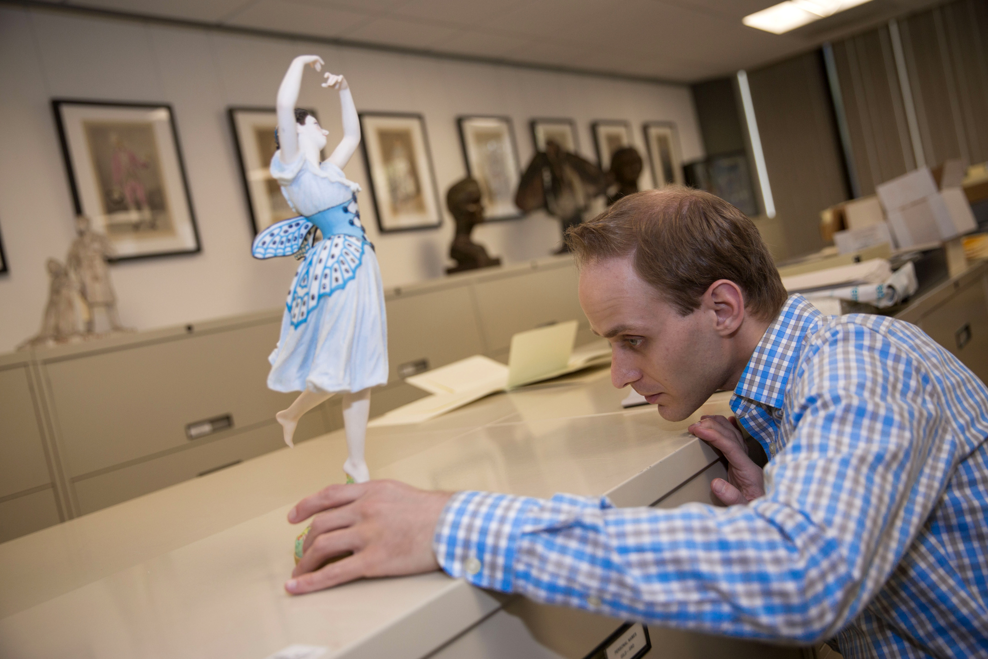 Dale Stinchcomb, Curatorial Assistant inspects a figurine by Jean Auguste Barre of the young French dancer Emma Livry (1842-1863) in "Le Papillon" (The Butterfly), within the Harvard Theatre Collections.