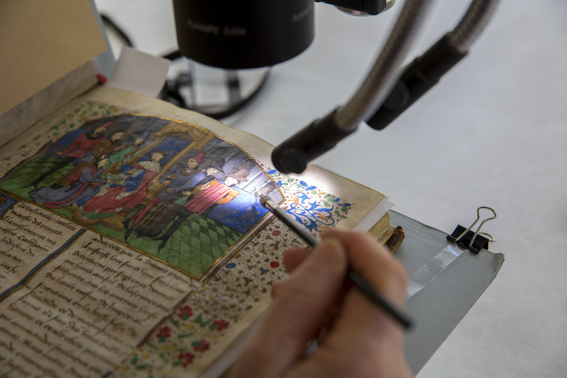 Book Conservator Catherine Badot-Costello utilizes a microscope to work on an illuminated, bound parchment manuscript from Houghton Library, dated 1464.