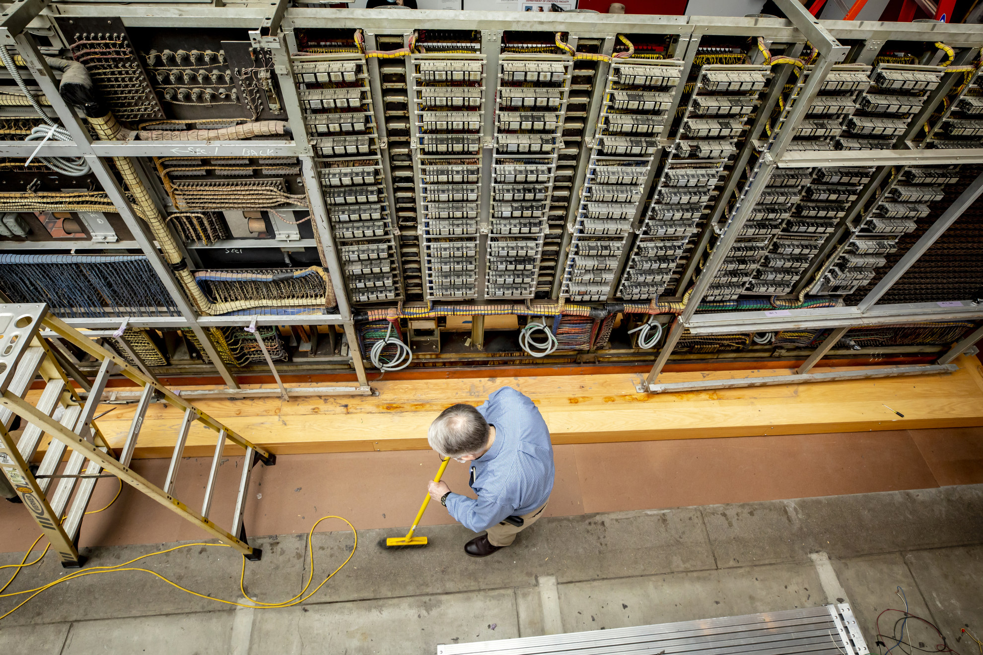 O.B. Hill Trucking and Rigging from Natick, MA and the Collection of Historical Scientific Instruments at Harvard are disassembling the iconic Mark 1 computer at the Science Center and moving it to the SEC where it will be reconstructed. A man sweeps around the partially taken apart computer still at the Science Center.