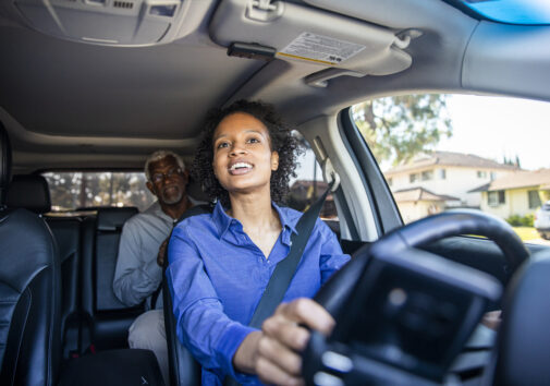 A young woman chauffeurs a passenger in her vehicle. Image credit: iStock