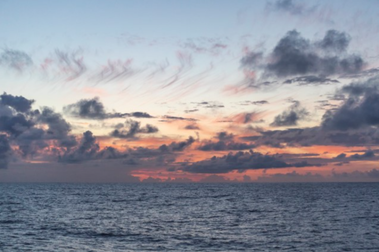 Scattered clouds drift above the sea during an orange-tinted sunset.