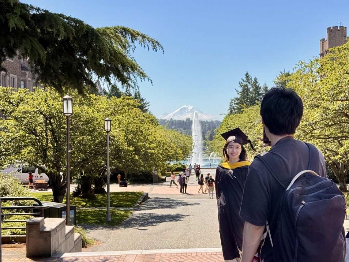 woman in graduation gown poses in front of view