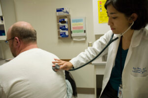 A physician holds the end of a stethoscope on a patient's back.
