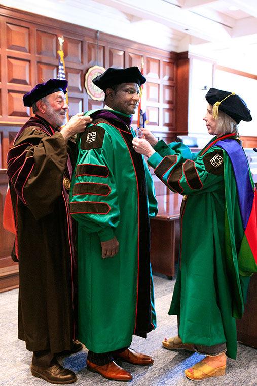 Stefanie Lindquist, the Nickerson Dean and professor of law at WashU Law, assists in placing the purple hood, indicating a degree in jurisprudence, over the Hon. Judge Edward Washington II during the ceremony on May 11. Washington’s former contracts professor Michael M. Greenfield, the George Alexander Madill Professor of Contracts & Commercial Law Emeritus, aided Dean Lindquist.
