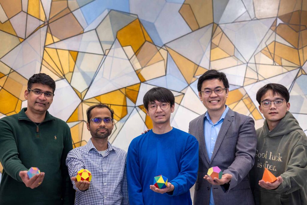 Five men stand in front of a wall, embellished with intersecting orange, gray, and blue polygons. Each man holds a large die-like object. From left to right, the men hold: a crystal with rhombus-shaped faces; a crystal with pentagonal and triangular faces; a crystal with 20 triangular faces; a crystal with 12 pentagonal faces, and a four-faced pyramid.