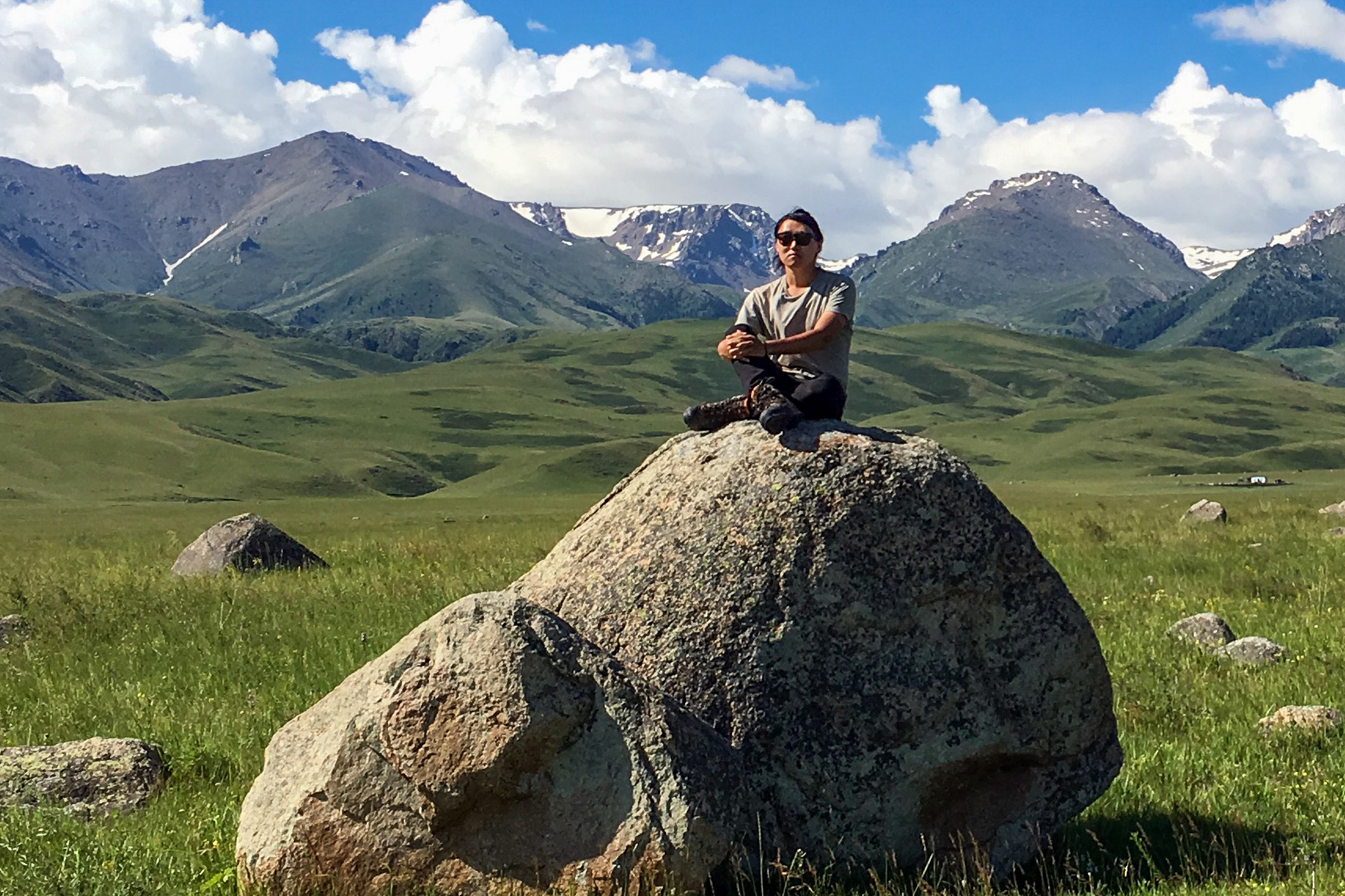 Alexander Mee-Woong Kim seated on a rock with mountains in the backdrop, in Kazakhstan.