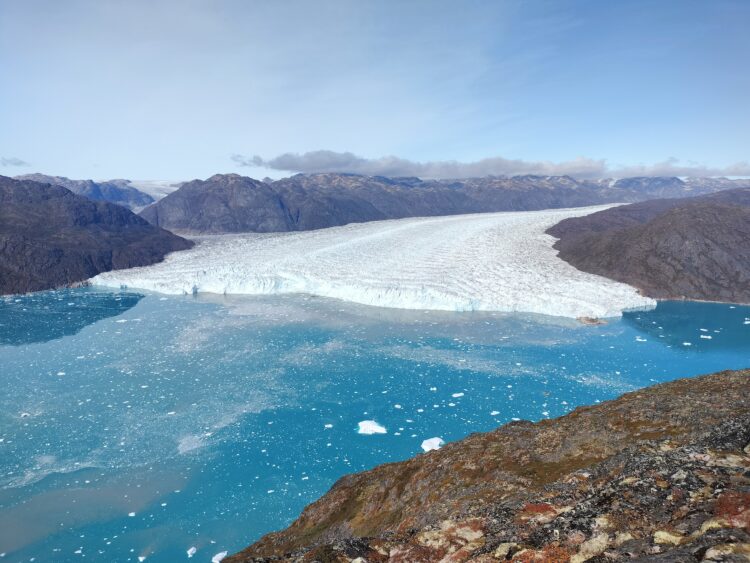 A landscape of a Greenlandic fjord with a massive glacier advancing from the background towards the foreground.