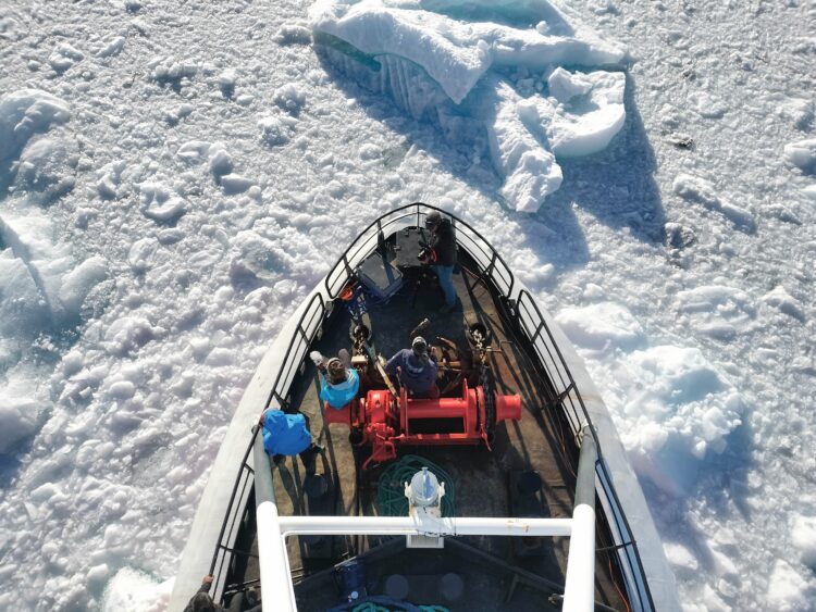 The bow of a boat from a bird's-eye viewpoint. Numerous dense icebergs surround the boat, obscuring the water entirely.