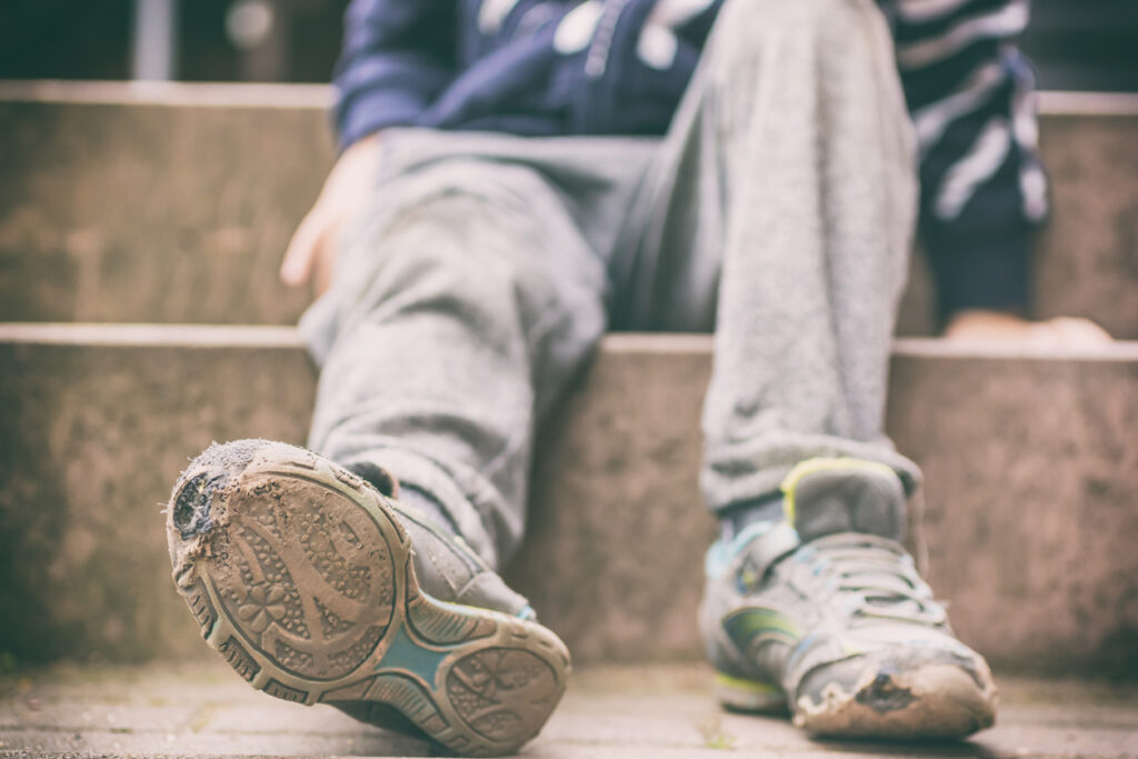 Worn-out footwear of an individual seated outdoors on steps. Image credit: iStock