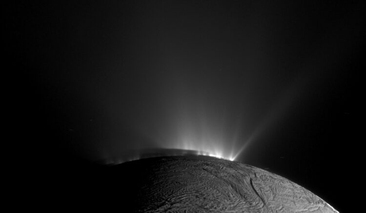 A monochrome image depicting the moon Enceladus. Brilliant jets of water burst forth from the subsurface.