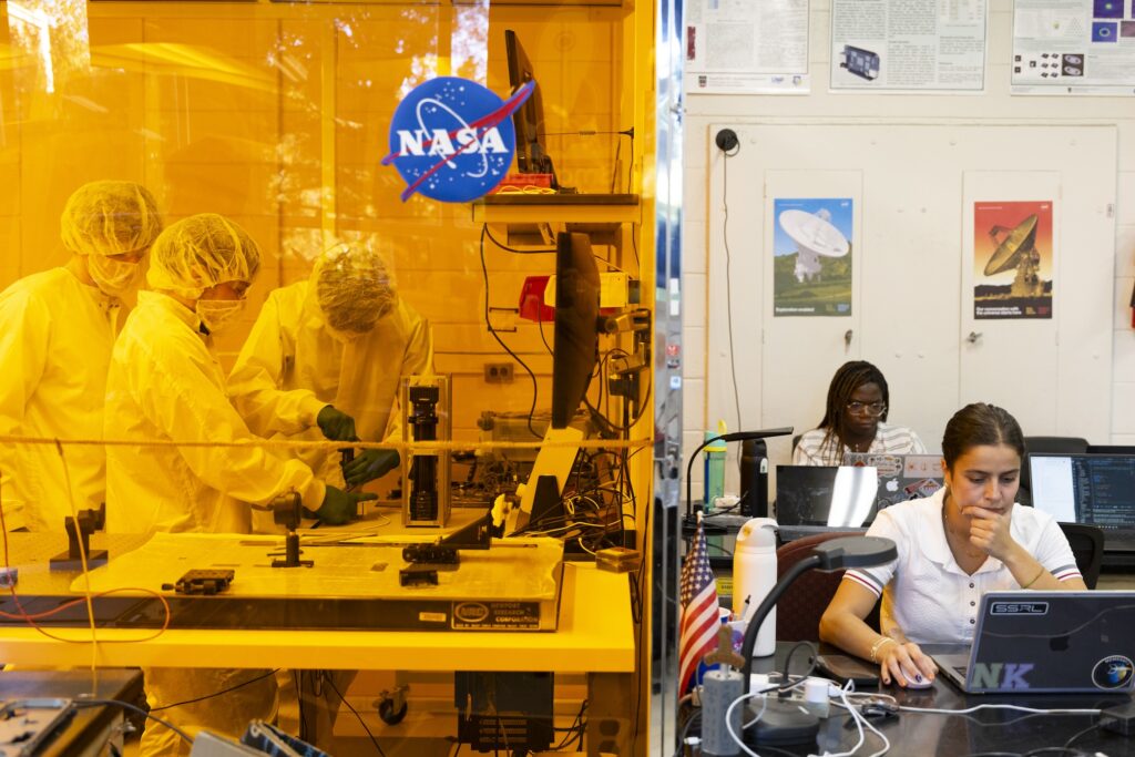 UGA students Gage Kelley, Nathaniel Leblanc and Nick Dagnino work in clean room suits assembling satellite equipment, while Anolita Hirsch and Nektaria Karagiannis work on laptops in the Small Satellite Research Laboratory.