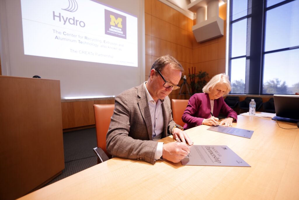 A man and a woman sign rectangular metal sheets at a conference table.