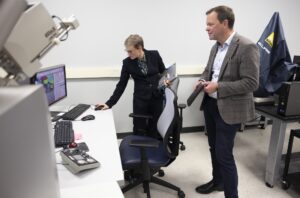 In a research lab, a woman stands in front of a computer and navigates while a man in a suit observes the demonstration.